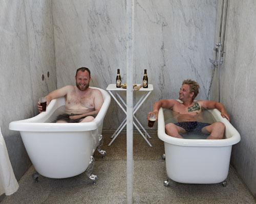 2 unge mænd nyder en afslappende tur i badekar med hver deres mørke øl mens de holder polterabend hos Sofiebadet på Christianshavn